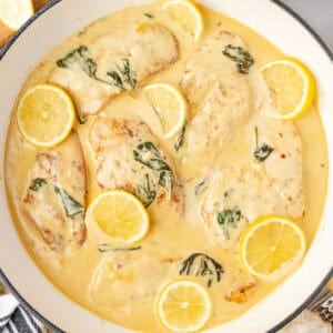 A skillet full of chicken in a lemon sauce with sliced lemons.