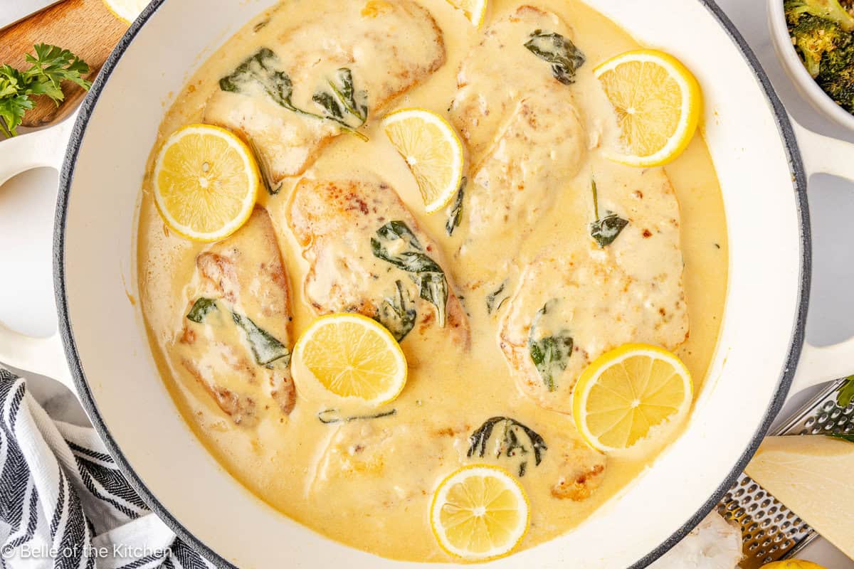A skillet full of chicken in a lemon sauce with sliced lemons.