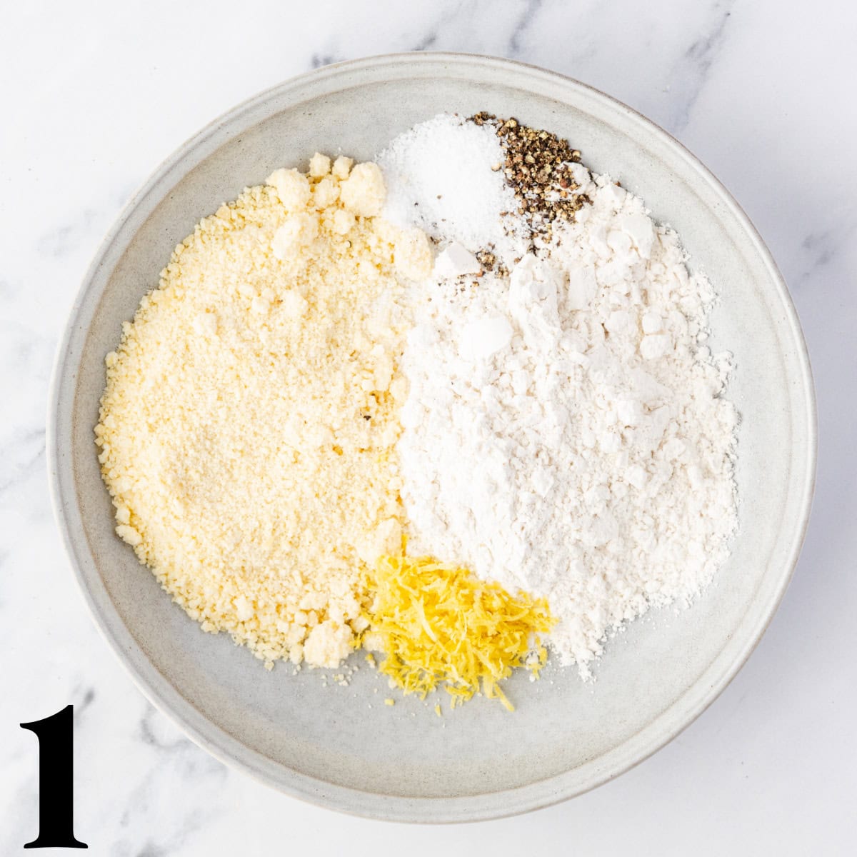 A white bowl of flour, cheese, spices, and lemon zest.