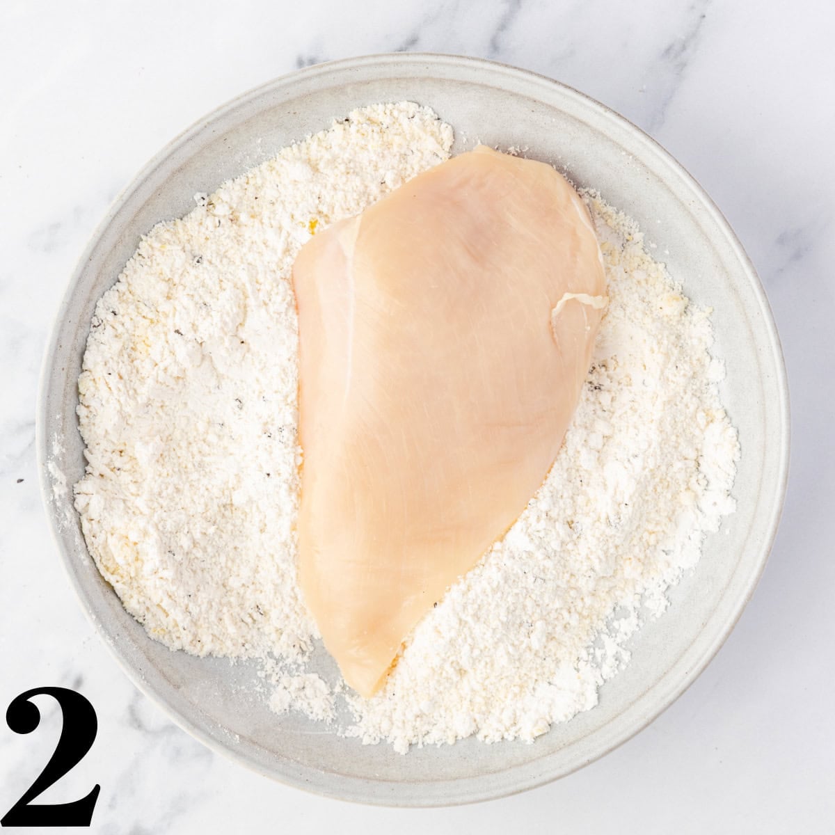 A piece of chicken being dredged in flour.