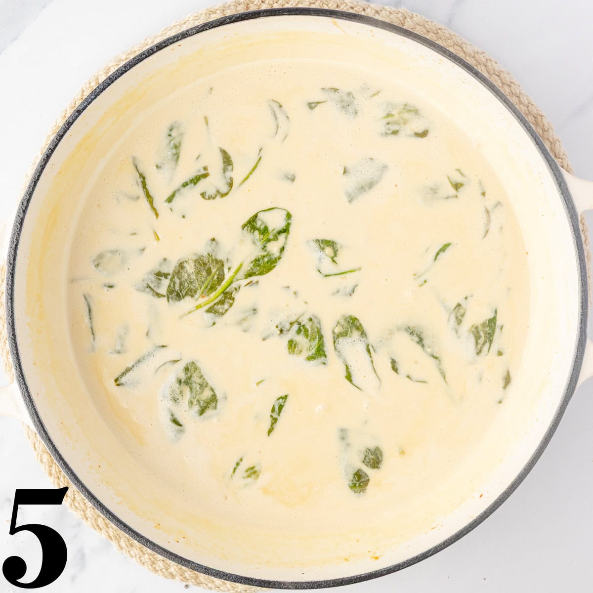 A skillet full of a cream sauce and spinach.