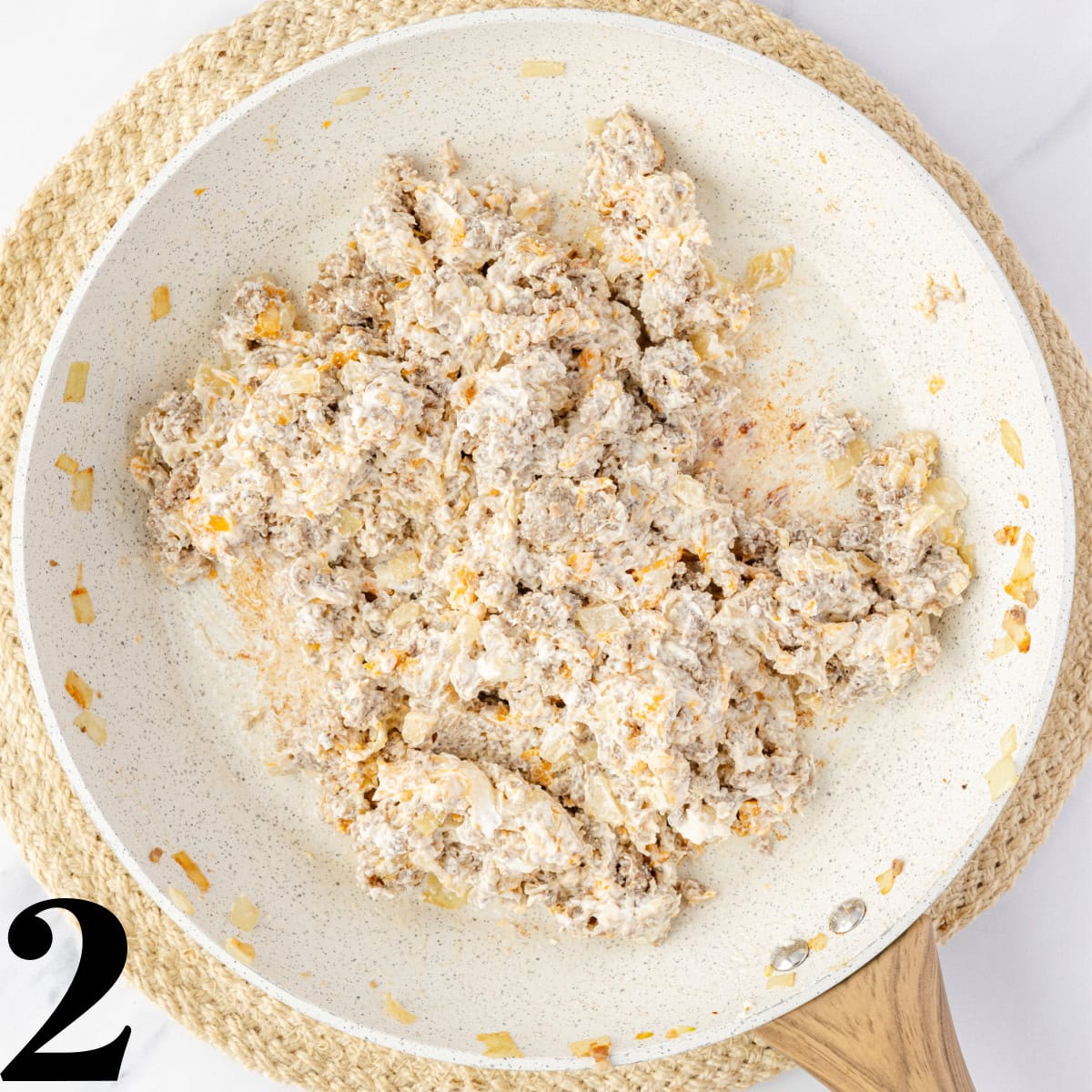 A skillet full of crumbled pork sausage mixed with cream cheese.