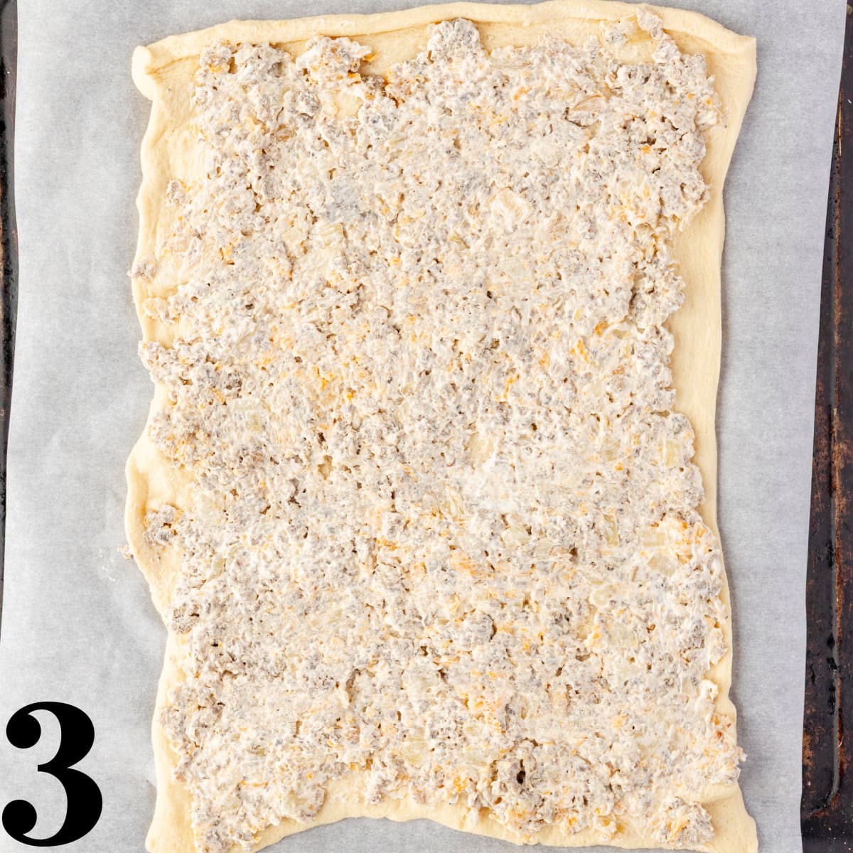 Sausage filling spread out on a crescent roll sheet on a cookie sheet.