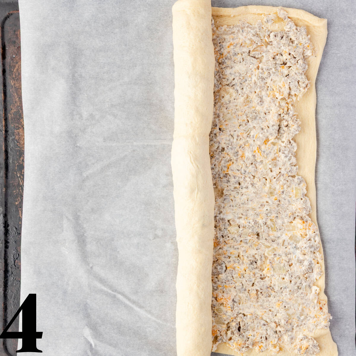 Crescent roll dough being rolled up with sausage inside.