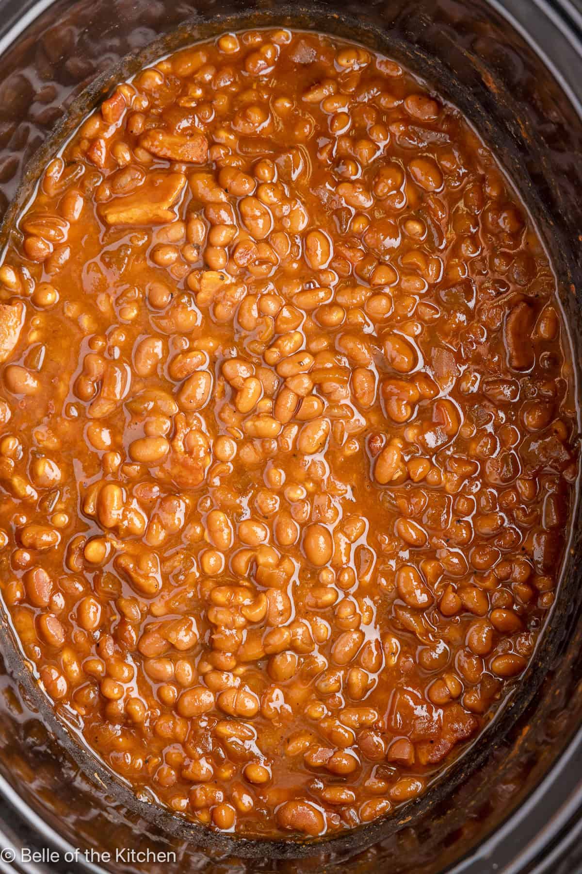 A black crockpot full of baked beans.