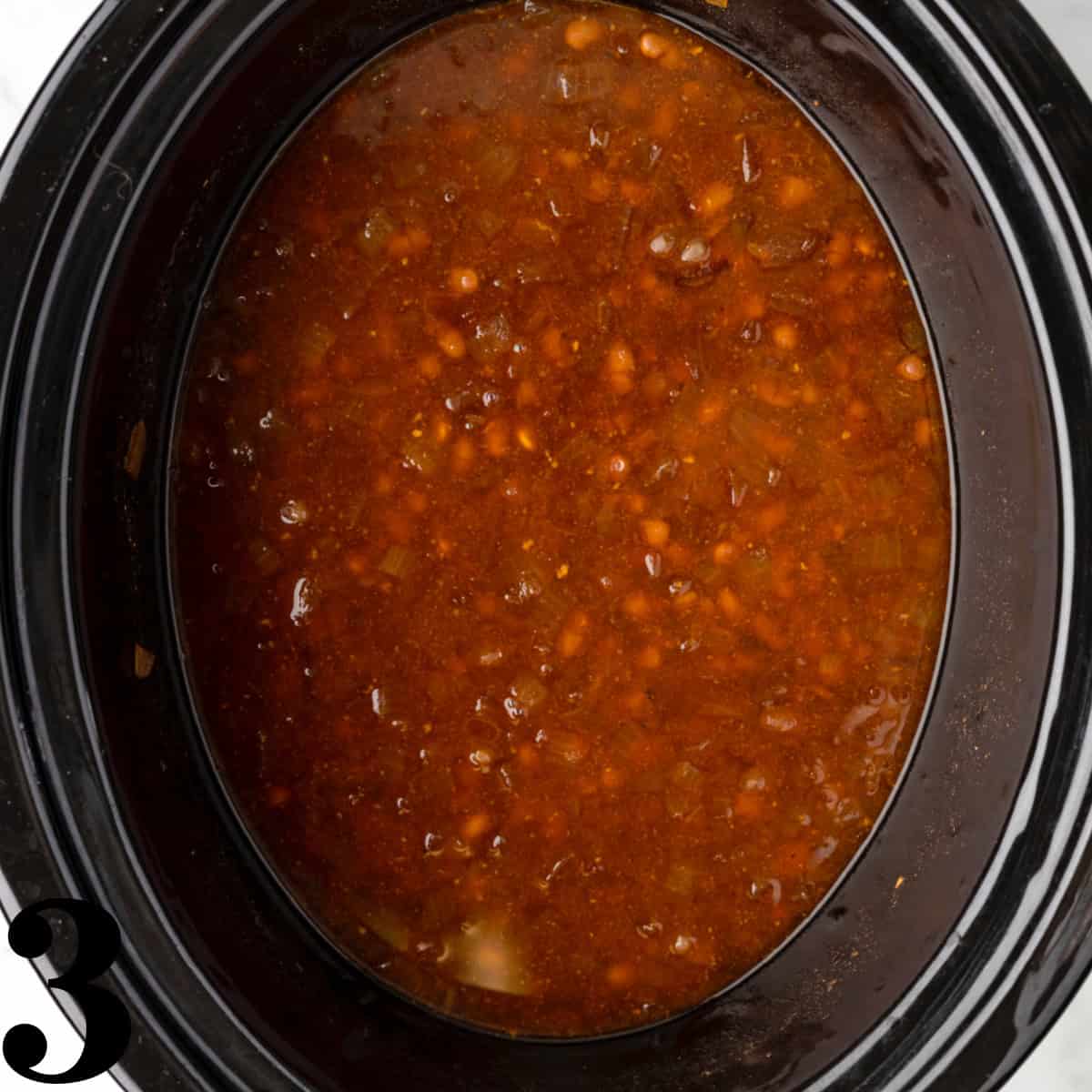 A black crockpot full of baked beans.