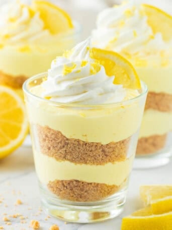 A cup of lemon cheesecake with whipped cream and a lemon on top.