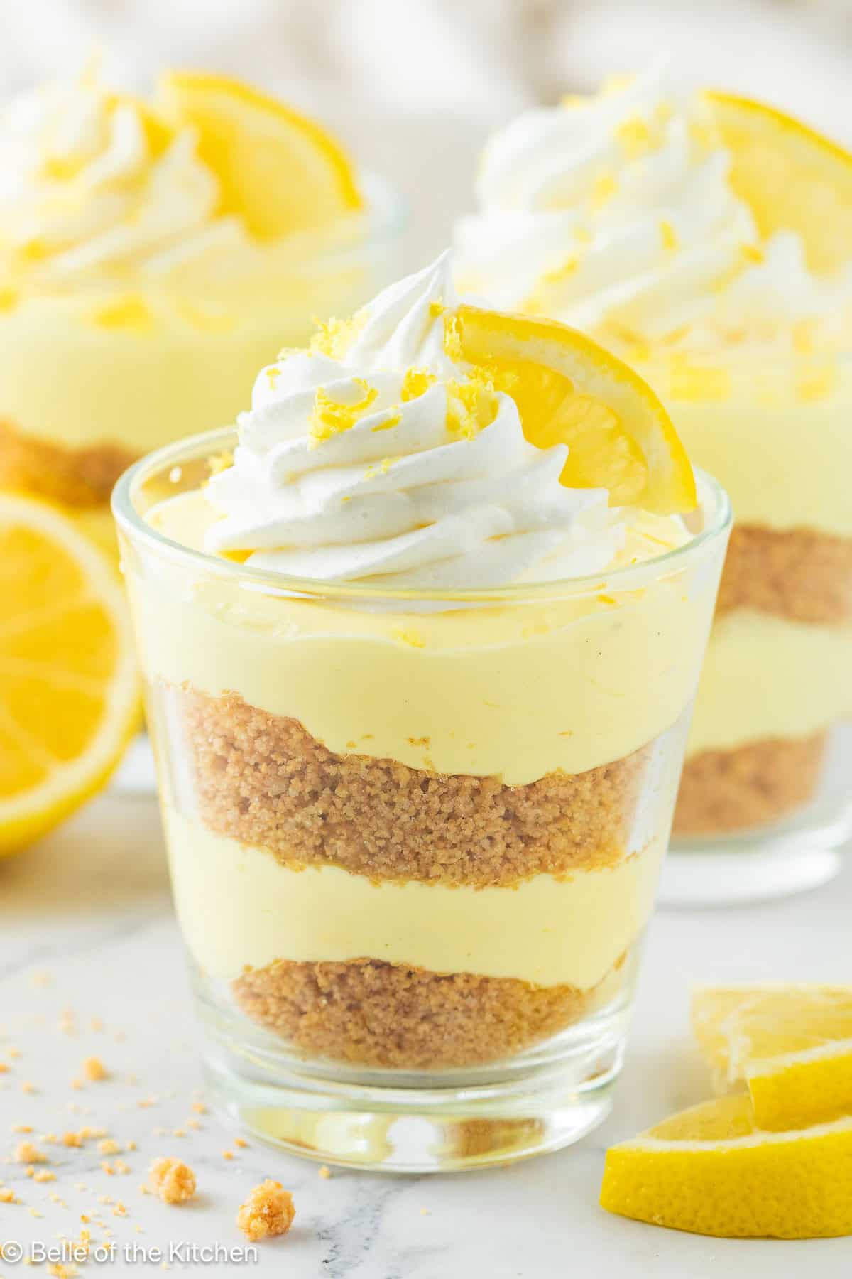 A cup of lemon cheesecake with whipped cream and a lemon on top.