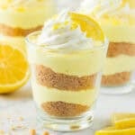 A cup of lemon cheesecake with whipped cream and a lemon on top.