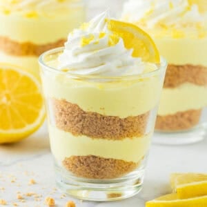 A cup of lemon cheesecake with whipped cream and a lemon on top.