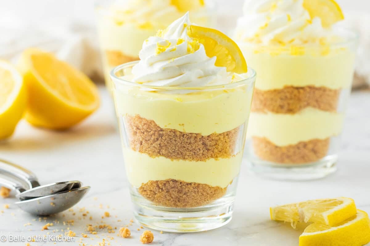 A cup of lemon cheesecake with whipped cream and a lemon on top.