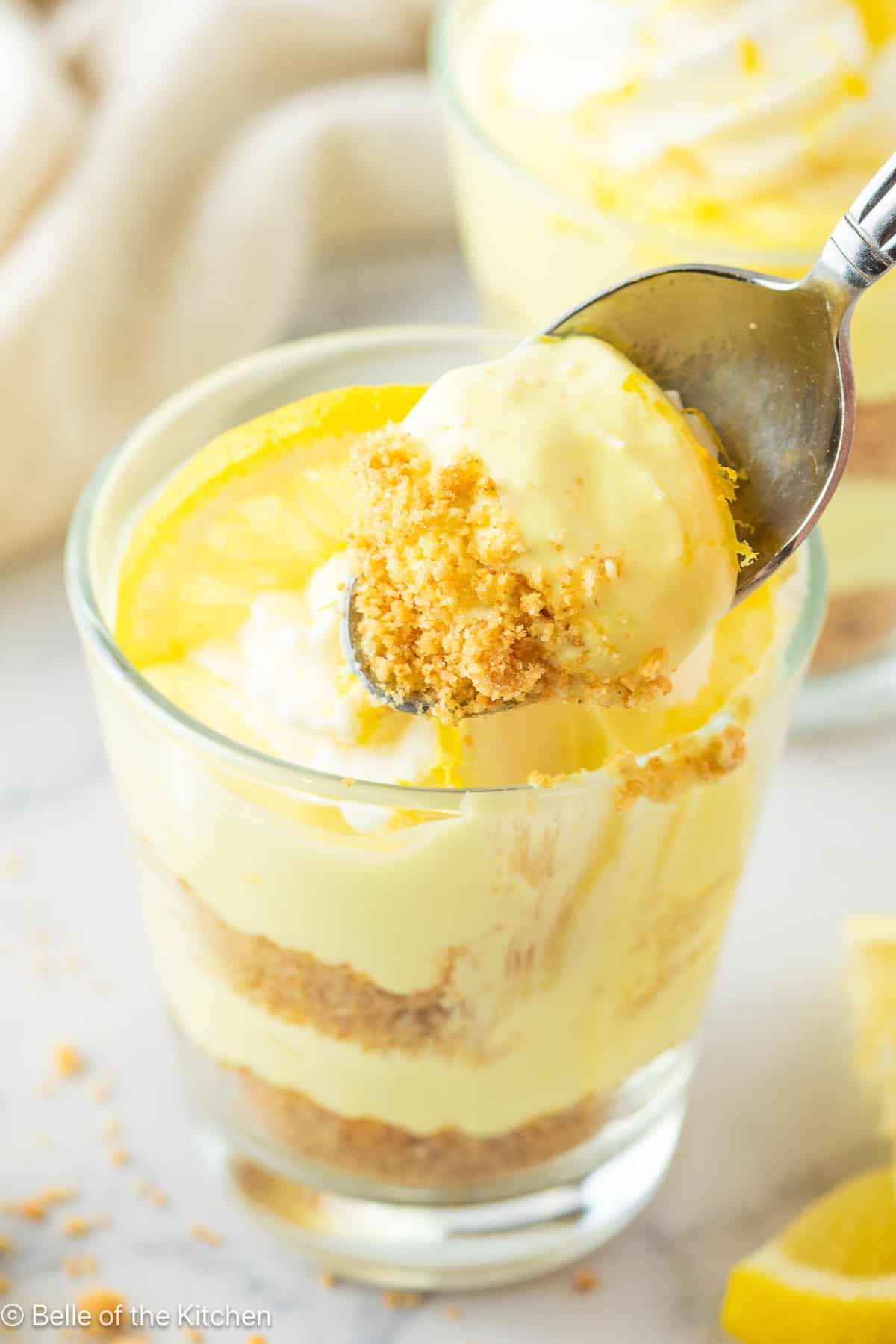 A spoon scooping lemon cheesecake from a cup.