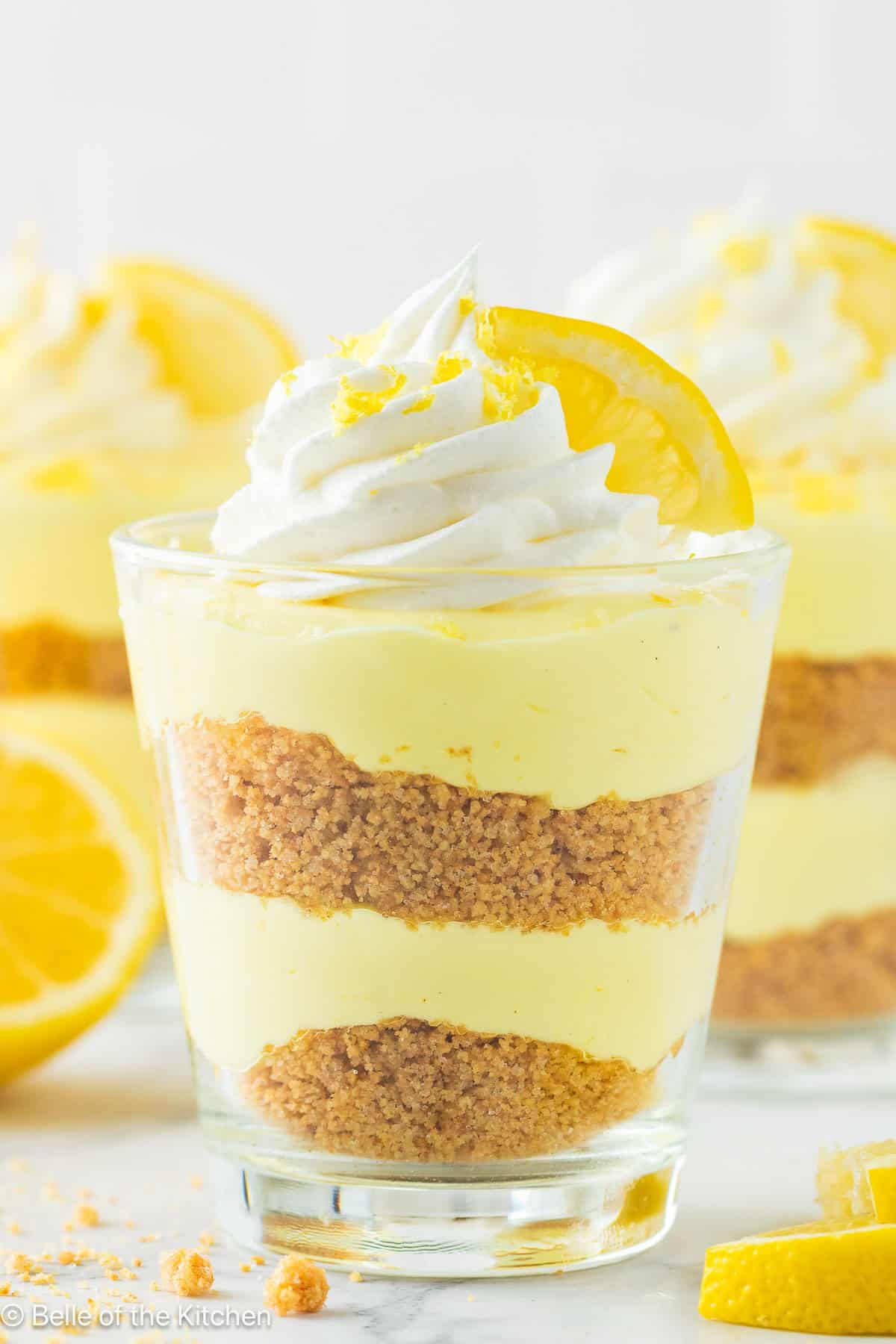 A cup of lemon cheesecake with whipped cream and a lemon on top.