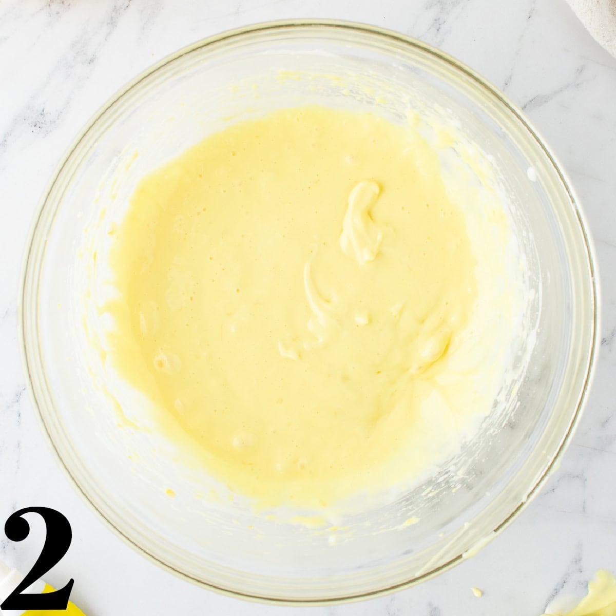 A glass bowl of yellow cheesecake batter.