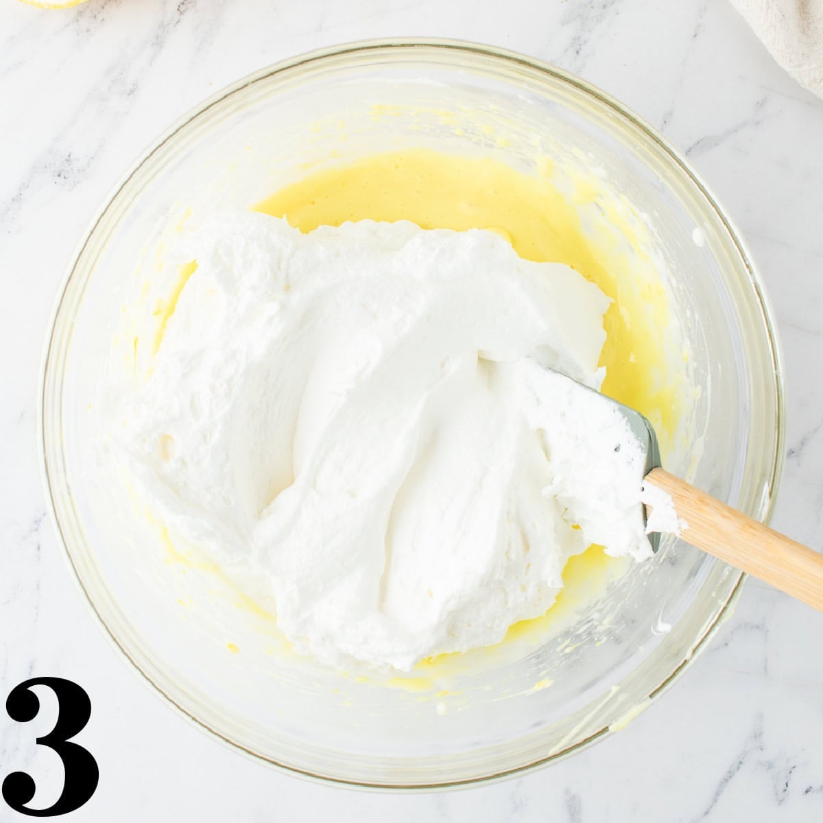 A glass bowl with whipped cream being folded into batter.