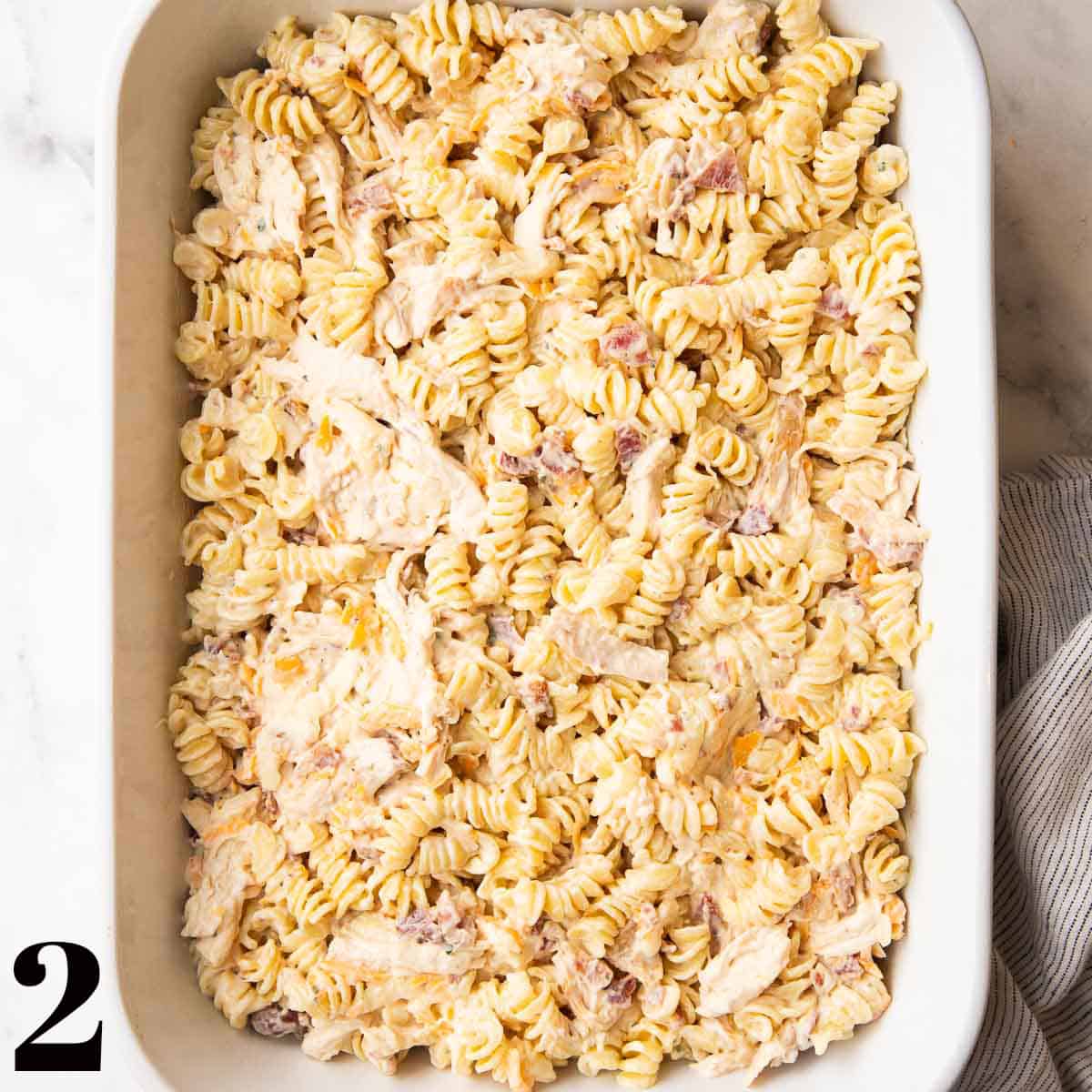 A white baking dish full of pasta, chicken, and bacon.