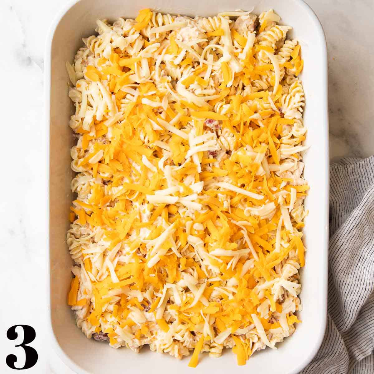 A white baking dish full of pasta, chicken, bacon, and cheese.