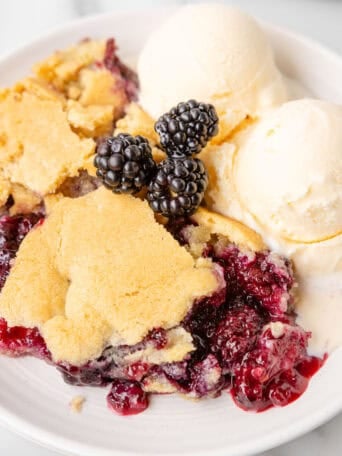 A bowl of blackberry cobbler with vanilla ice cream on top.