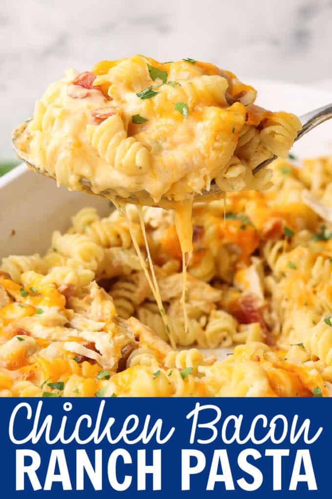 A spoon lifting food from a white baking dish full of pasta, chicken, bacon, and cheese.