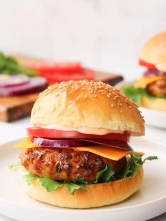 A turkey burger with a bun and toppings on a white plate.