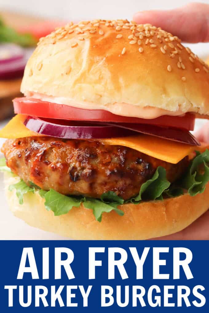 A hand holding a turkey burger with a bun and toppings above a white plate.