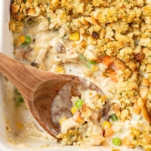 A wooden spoon scooping up chicken and stuffing casserole.