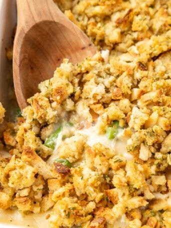 A wooden spoon scooping up chicken and stuffing casserole.