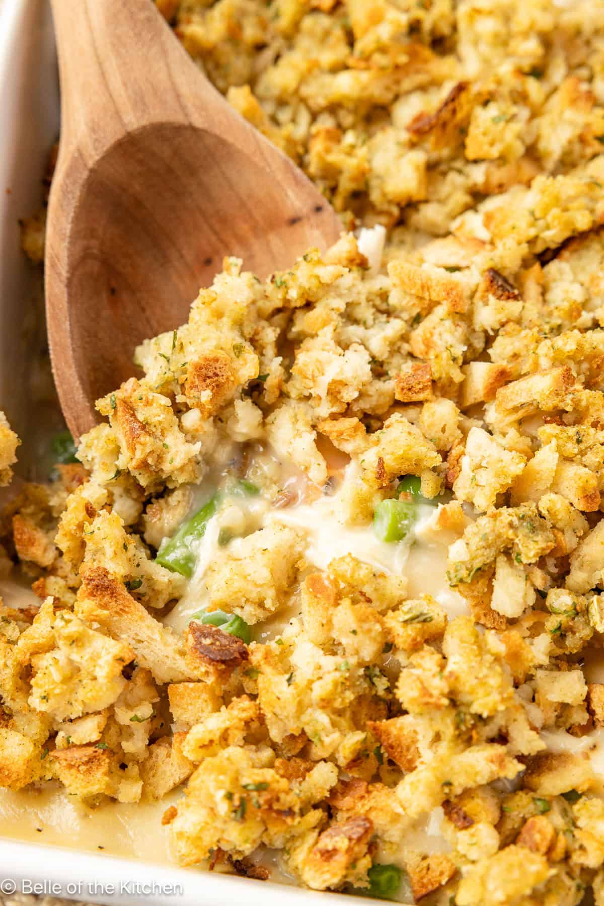 A wooden spoon scooping up chicken and stuffing casserole.
