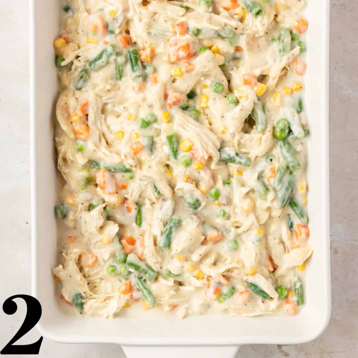 A white baking dish full of chicken casserole with vegetables.