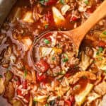 A wooden spoon scooping up cabbage roll soup from a crockpot.