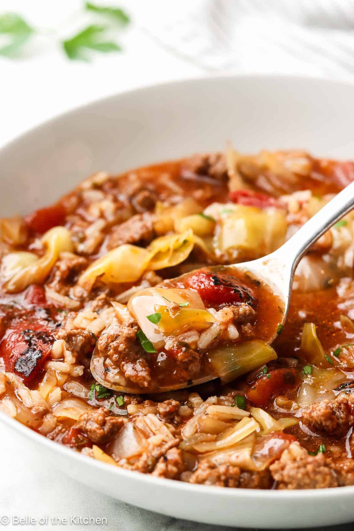 A spoon scooping cabbage roll soup from a white bowl.