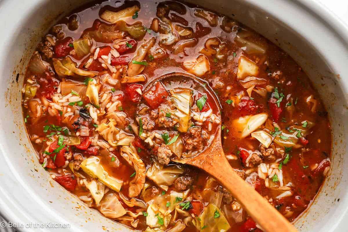 A wooden spoon scooping up cabbage roll soup from a crockpot.