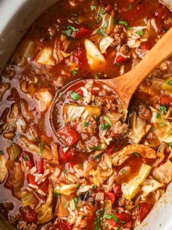 A wooden spoon scooping up cabbage roll soup from a crockpot.