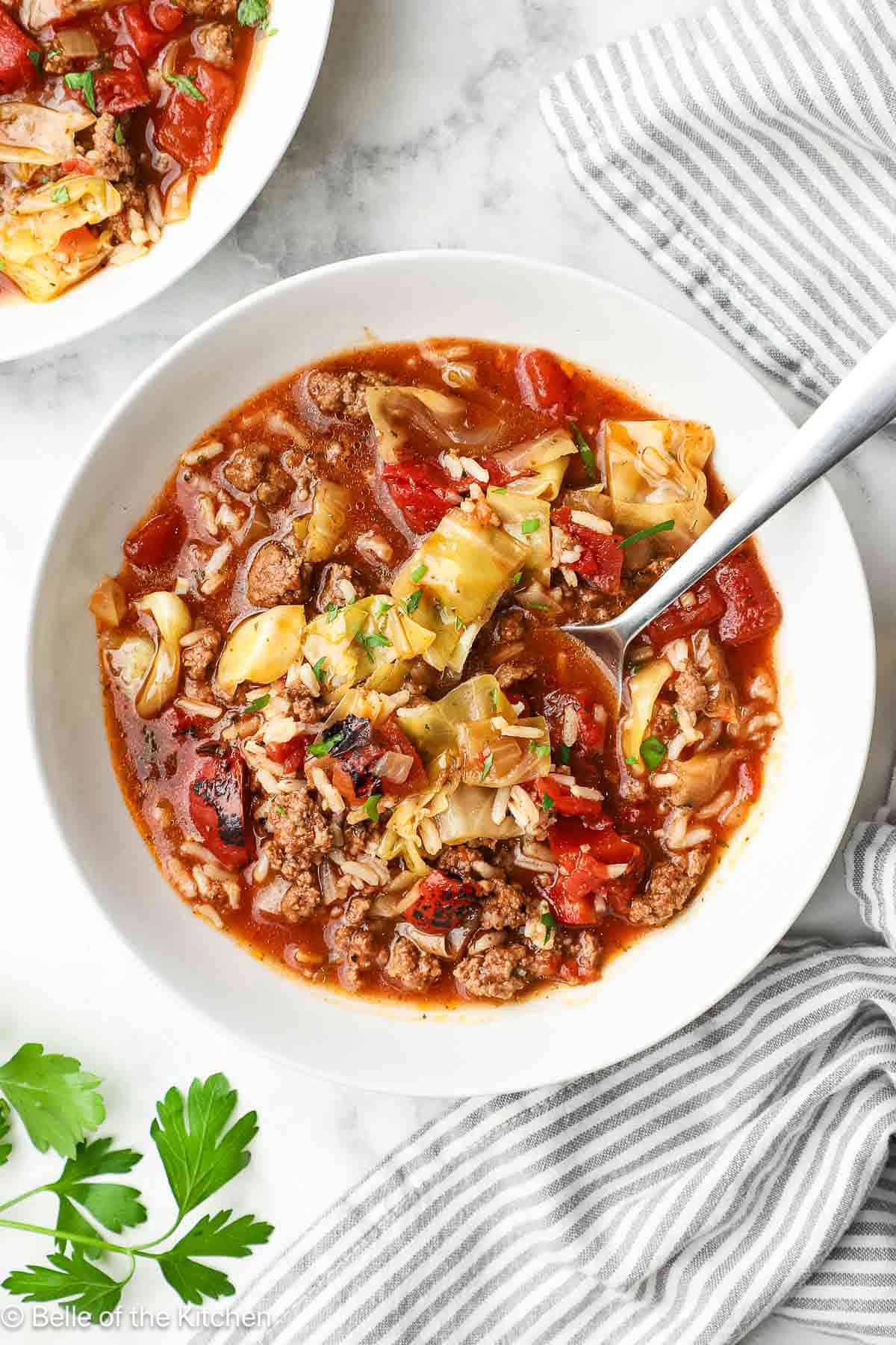A spoon scooping cabbage roll soup from a white bowl.