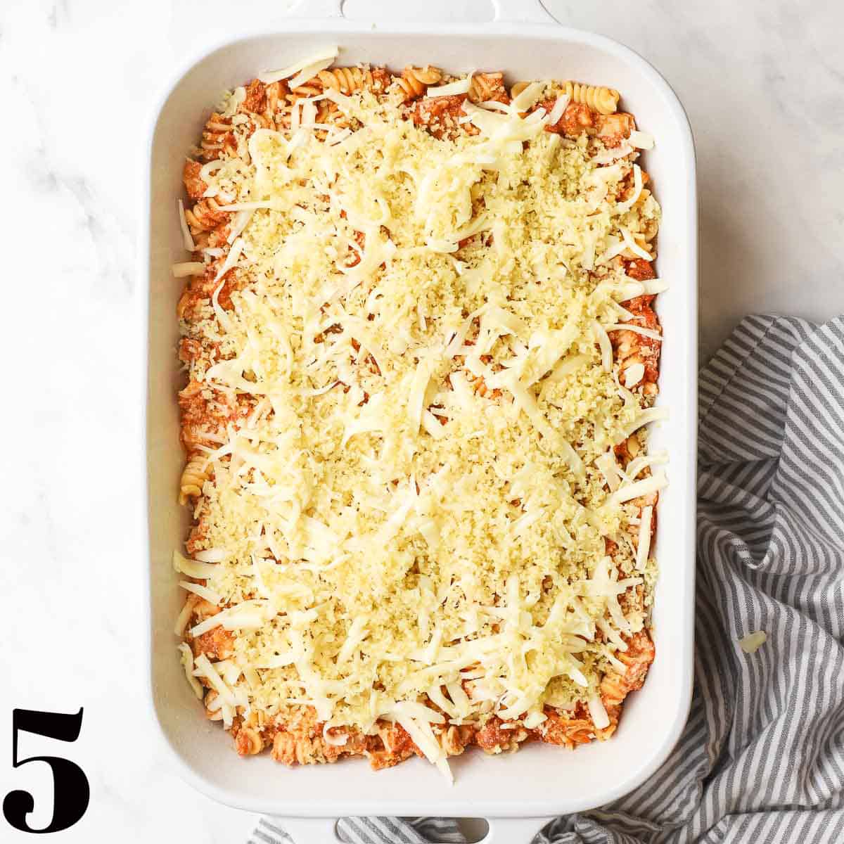 A white baking dish full of pasta and sauce topped with cheese.