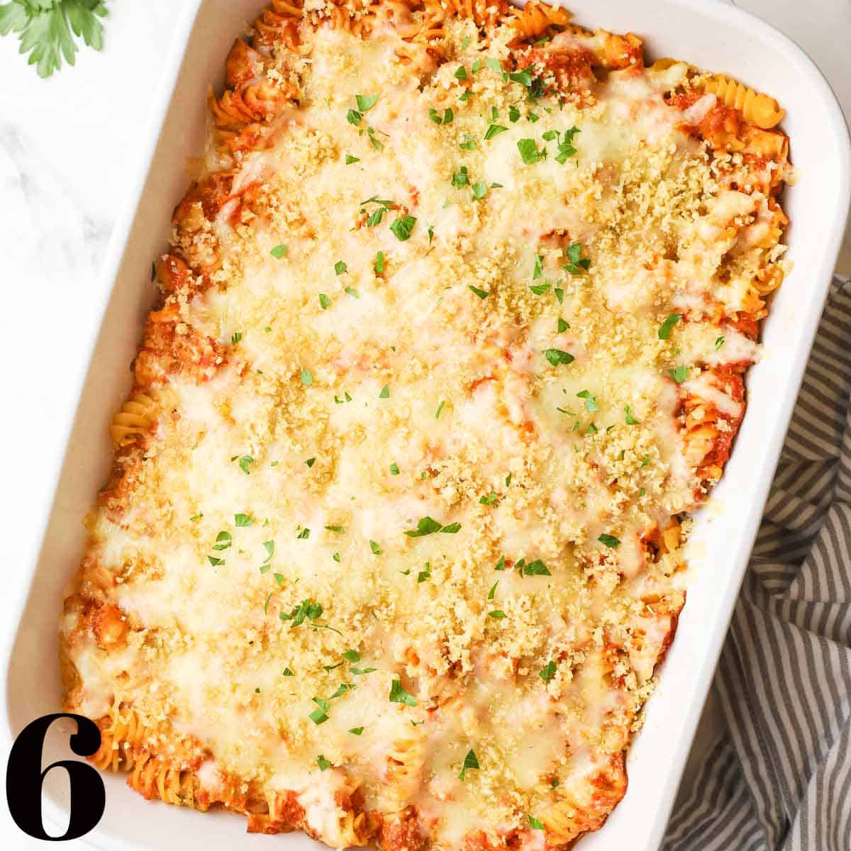 A white baking dish full of pasta and sauce topped with cheese.