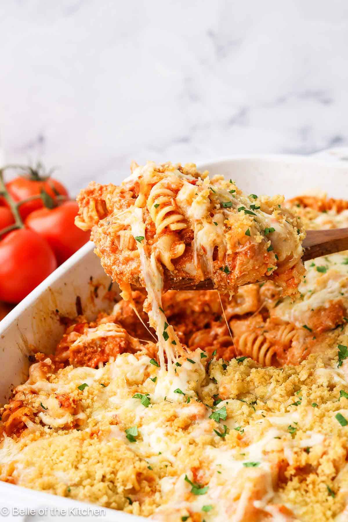 A baking dish full of chicken parmesan pasta with a wooden spoon dipping some out.