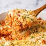 A baking dish full of chicken parmesan pasta with a wooden spoon dipping some out.