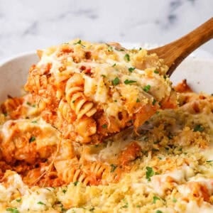 A baking dish full of chicken parmesan pasta with a wooden spoon dipping some out.