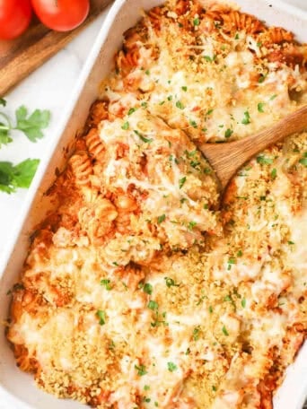 A baking dish full of chicken parmesan pasta with a wooden spoon dipping some out.
