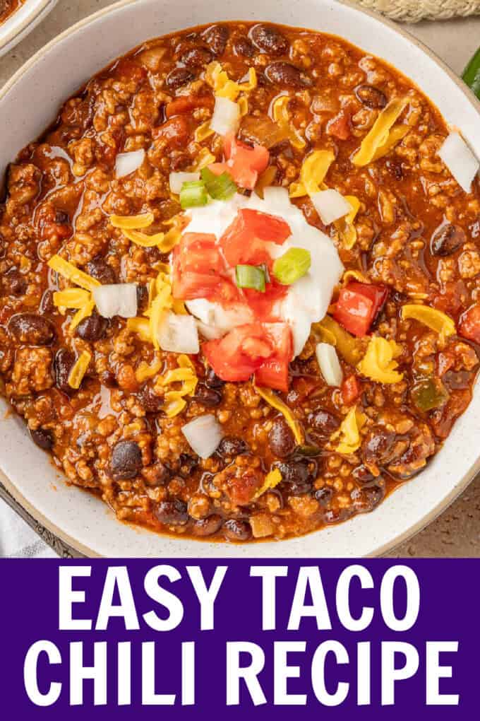A white bowl of chili topped with sour cream, tomatoes, onions, and cheese.