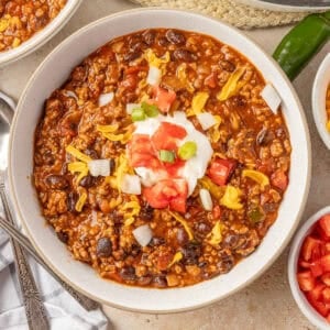 A white bowl of chili topped with sour cream, tomatoes, onions, and cheese.