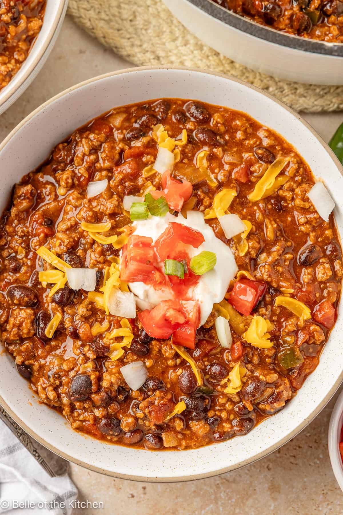 A white bowl of chili topped with sour cream, tomatoes, onions, and cheese.
