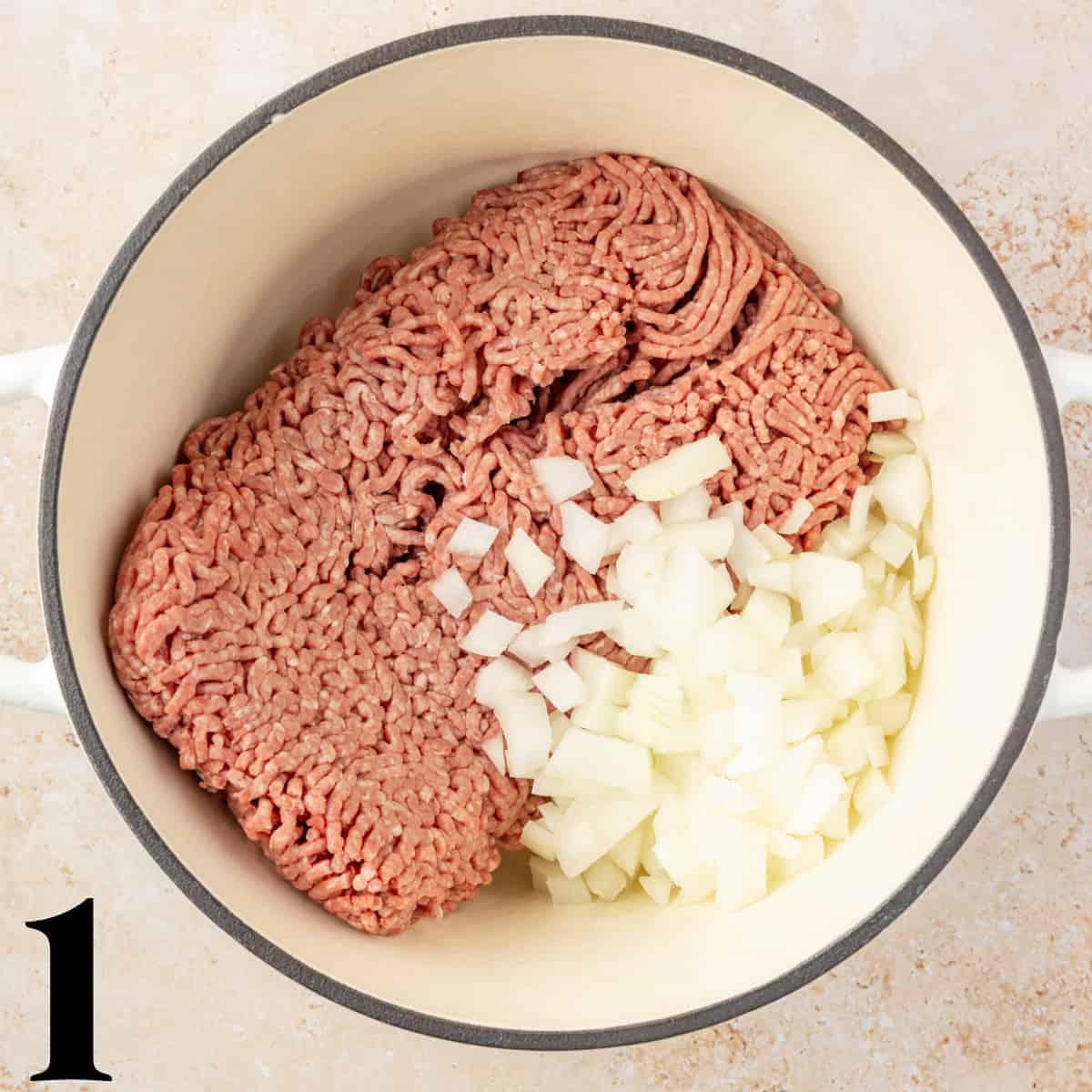 A dutch oven full of raw ground beef and diced onions.