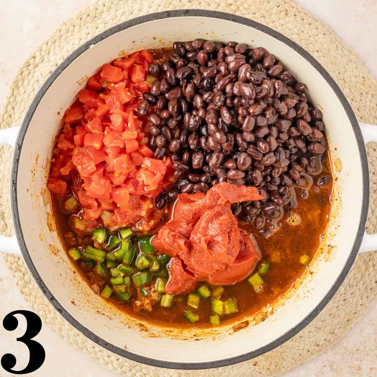 A dutch oven full of black beans, tomatoes, tomato paste, and jalapenos.